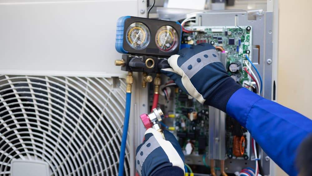 HVAC technician using manifold gauges to check refrigerant pressure during an AC tune-up and maintenance service.